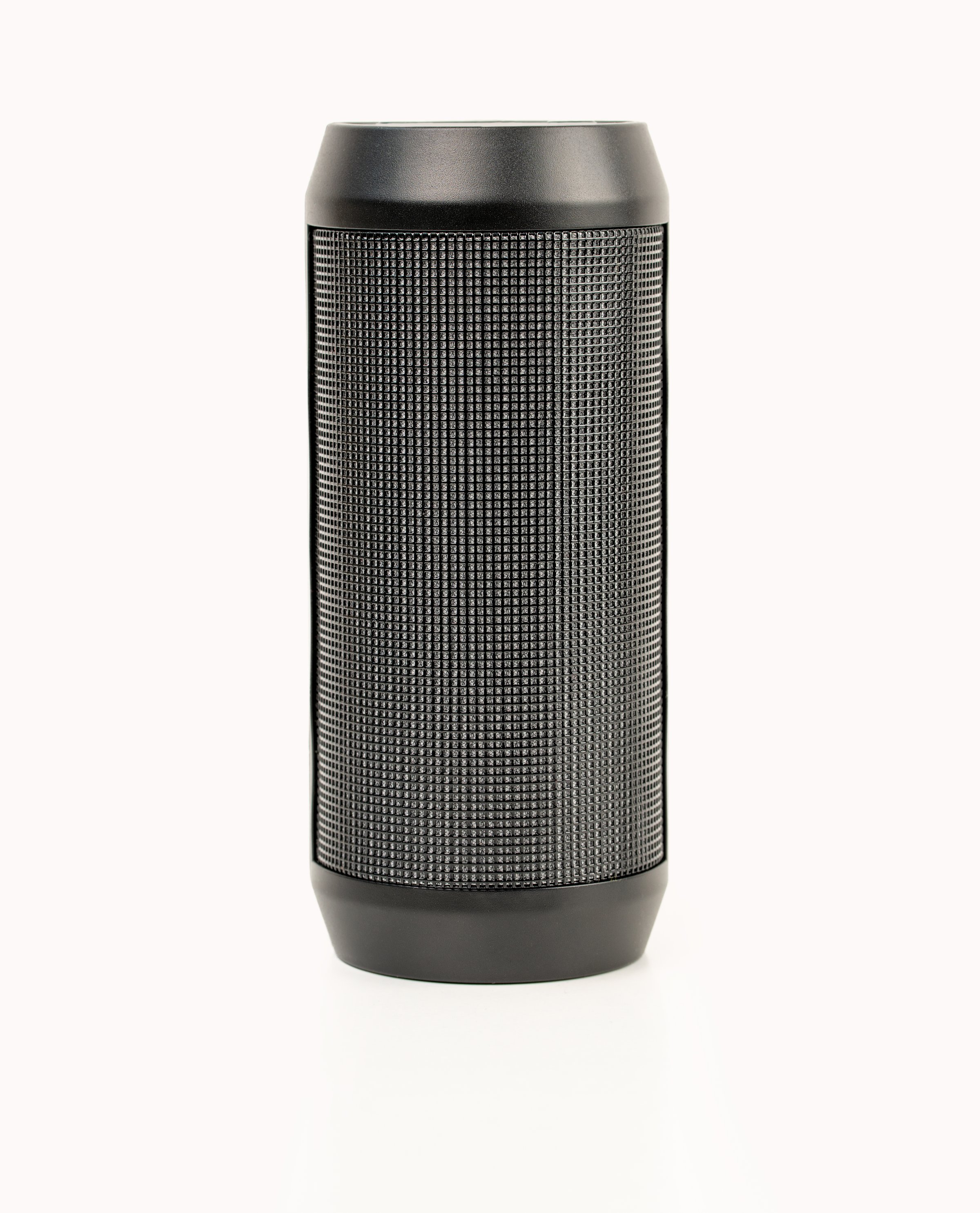 Black portable wireless speaker isolated on white background. Mobile loudspeaker black color with ribbed texture and push control buttons.Vertical position.Close-up.